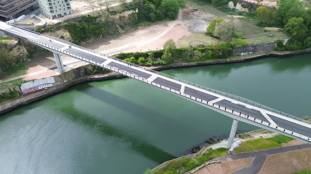 A slow left-orbiting drone shot circles the Keel Crossing, a sleek pedestrian and cycling bridge spanning the green River Wear in Sunderland, northeast England.