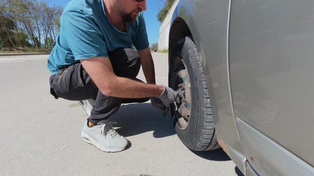 Man unscrewing car wheel bolts with a lug wrench outdoors