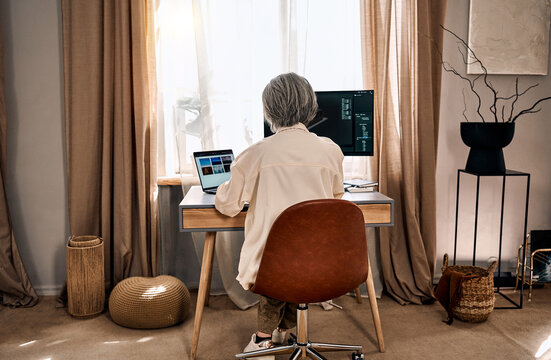 Senior woman working from home at desk with computer monitors.