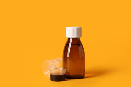 Bottle of cough syrup and measuring cups on orange background