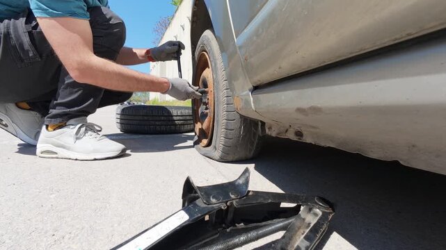 Man changing a flat tire with a lug wrench on a car