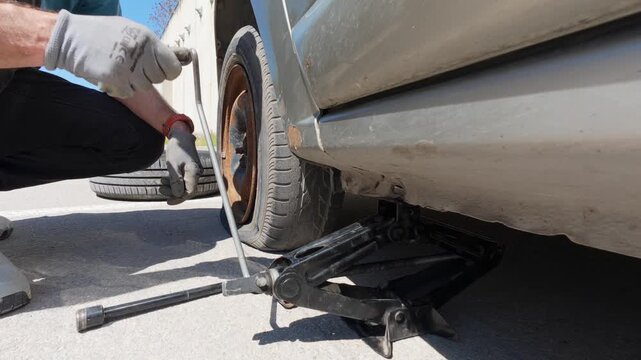 Man lifting car with scissor jack to change a flat tire