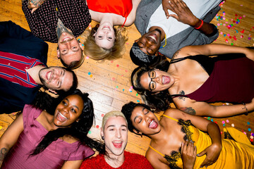 Fototapeta premium A diverse group of people lying in a circle on a wooden floor, smiling and laughing, surrounded by colorful confetti.