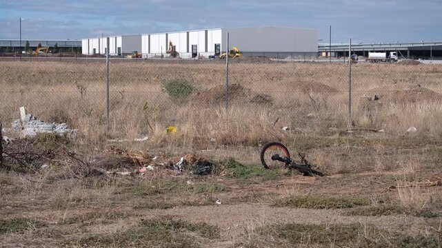 Abandoned bicycle in a neglected vacant lot in the industrial precinct of Truganina, Melbourne. A wire mesh fence separates the wasteland from a logistics warehouse or industrial distribution center