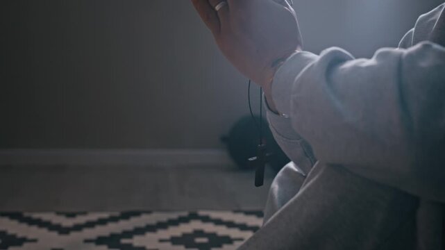 Cropped shot of unrecognizable woman holding cross in prayer while sitting on floor at home