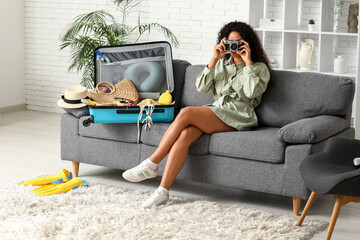 Beautiful young woman with camera unpacking summer clothes from suitcase at home © Pixel-Shot