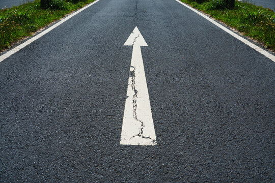 An asphalt road stretches into the distance with a painted white arrow, symbolizing motivation, progress and the concept of continuous growth and forward movement.