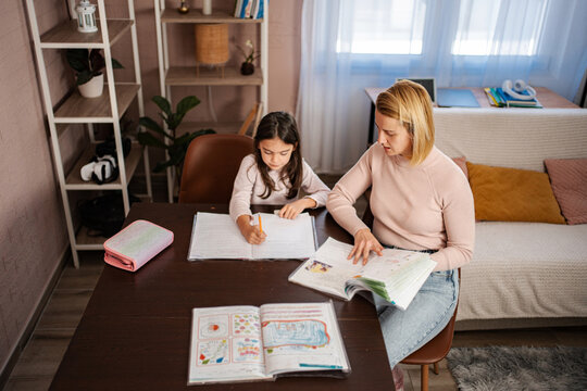 Mother helping daughter with homework during homeschooling lessons