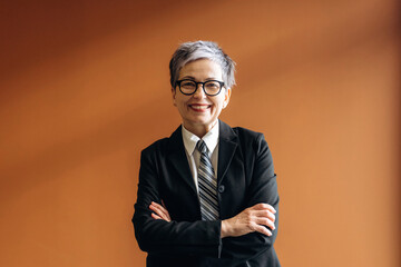 Businesswoman with short gray hair and glasses wearing a black suit and tie, standing confidently...