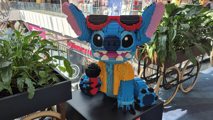 Naklejka premium A large LEGO sculpture of Stitch wearing sunglasses and a yellow shirt, holding a microphone in a Park Lake shopping mall. Picture taken on May 7, 2026 in Bucharest, Romania.