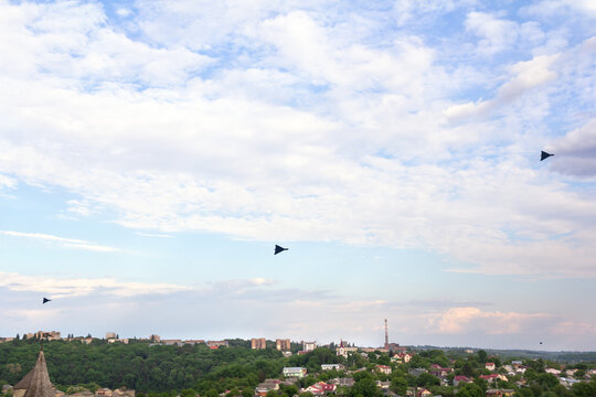Shahed type kamikaze drones flying in blue sky with clouds above the city, black loitering munition, unmanned aerial vehicle (UAV) in flight