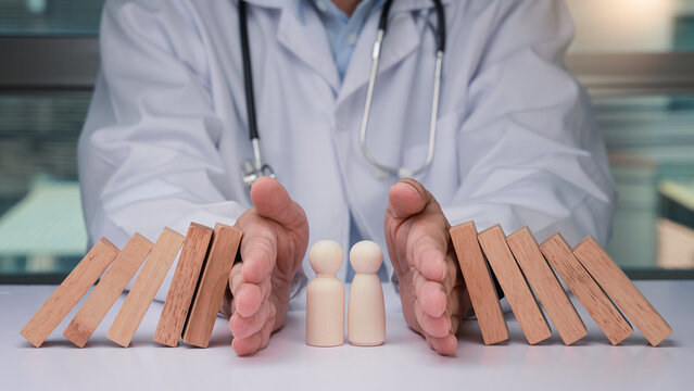 Caring doctor provides secure healthcare and protective insurance campaign stopping falling block to keep wooden family figure safe from harm