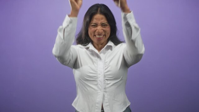 Woman clenching fists near face in a white shirt inside a purple studio backdrop, mid sequence of raised arms and smiling expressions; relief celebration.