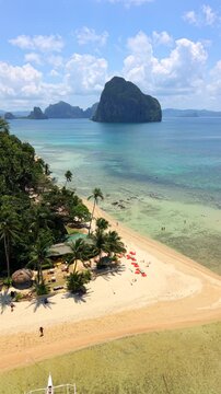 Aerial drone view of Las Cabanas Beach in El Nido, Palawan, Philippines featuring tropical palm trees, turquoise water, sandy shoreline, and scenic island landscape.