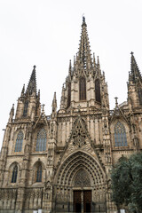 Fototapeta premium Front facade of Barcelona Cathedral in Spain with towering Gothic spires and detailed medieval architecture under cloudy sky in historic city center