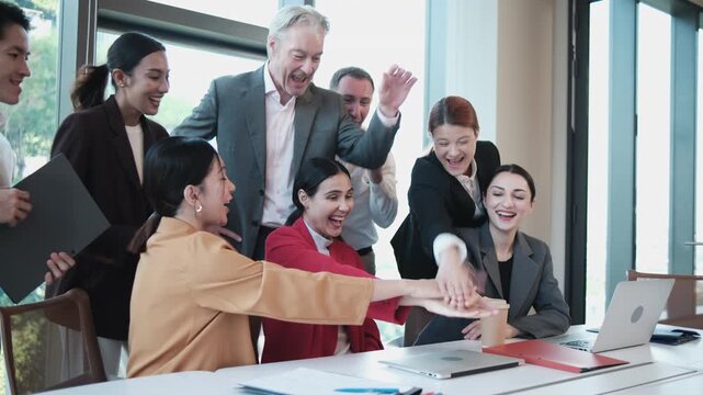 Young female CEO and multiracial partner team are happy and cheerful, joining hands after finishing business online conference on laptop, united with aspiration of achieving goal in executive meeting.