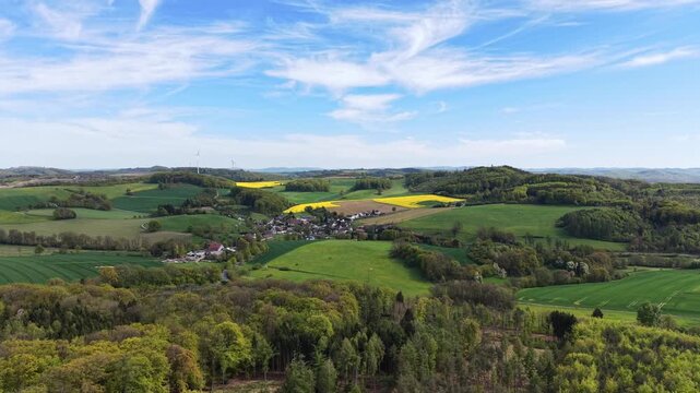 Beautiful panorama of rolling hills, a small village, and forests under a blue sky with clouds