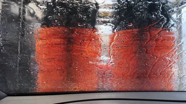 View from inside a car as vibrant orange brushes rotate against a wet windshield at a car wash. Useful for automotive or cleaning industry content.