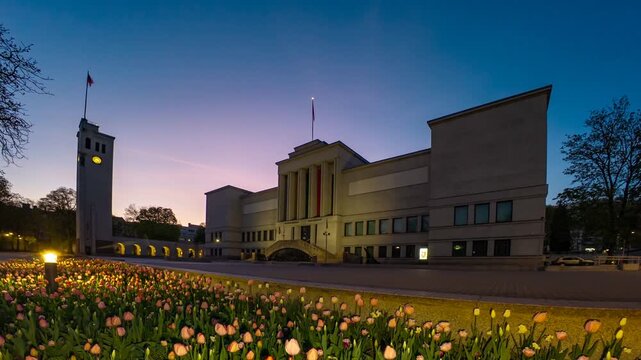 Famous lithuanian museum transitioning from sunset to night with illuminated tulips in the foreground