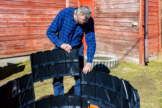 Installation modular compost bin with interlocking panels, farmer assembles parts by inserting one into other and clicking them together.