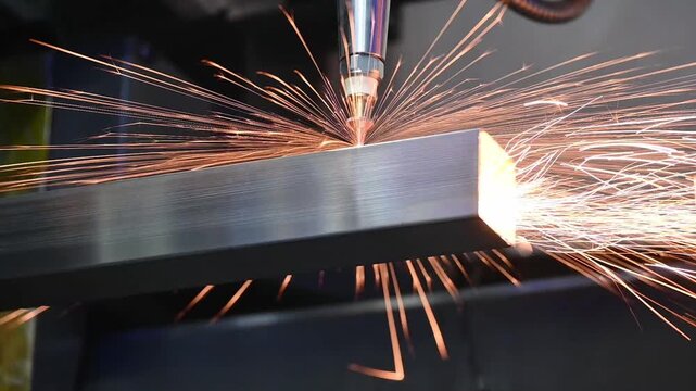 Slow motion video of fiber laser cutting machine engraving and slicing a metal square tube with intense sparks.