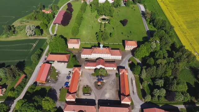 Aerial view of a historic estate complex with red-tiled roofs and white buildings surrounded by lush green trees and fields in Hofgeismar, Hessen, Germany.