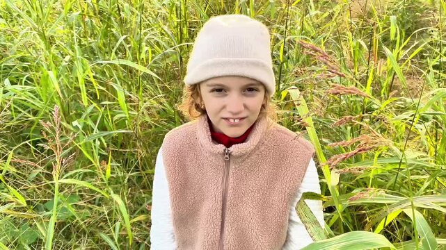  Close-up of a smiling young girl with a gap tooth sitting in a tall grass field.