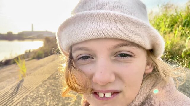 Close-up portrait of a cheerful young girl in a knit hat outdoors at sunset