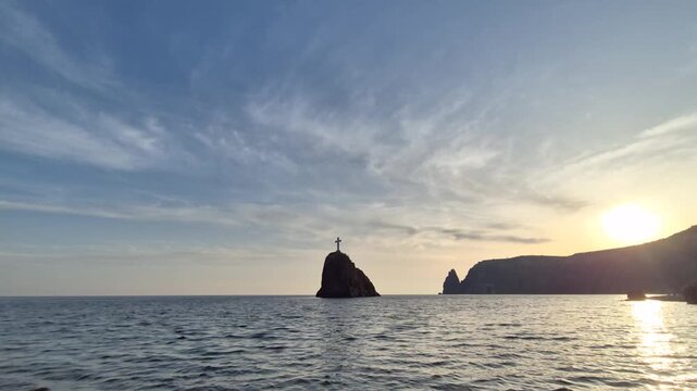 Sunset timelapse cross sea silhouette of a rocky island with a religious cross in the ocean during a golden sunset at cape fiolent