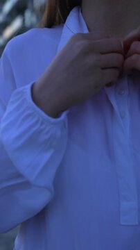 Woman buttoning shirt young woman adjusting her white linen blouse outdoors during twilight for an elegant evening outing