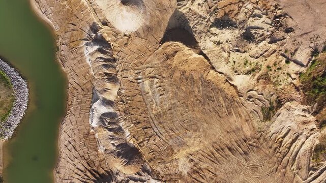 Aerial view of a sand quarry with tire tracks next to a green river in Uckermark, Brandenburg, Germany.
