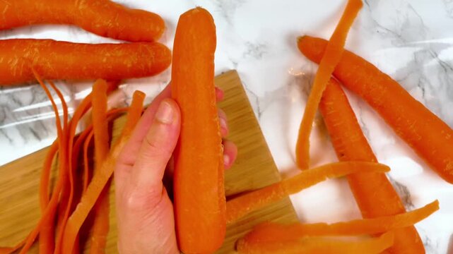 woman hand peeling fresh raw carrots with vegetable peeler on wooden board