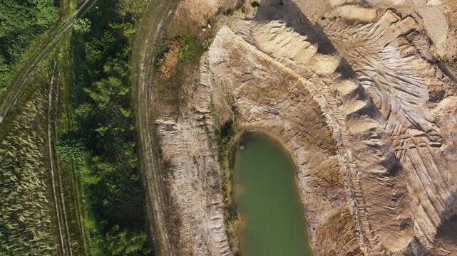 Aerial view of a sand quarry featuring tire tracks, a small green pond, and surrounding lush vegetation in Uckermark, Brandenburg, Germany.