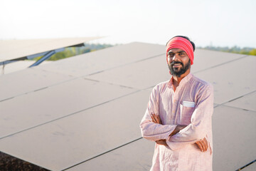 A confident indian farmer or rural worker stands in front of solar panels at agriculture field © PRASANNAPIX