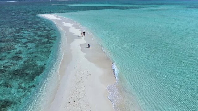 Aerial view of people walking along a narrow white sandbank surrounded by turquoise ocean water and coral reefs in Thoddoo, Alif Alif Atoll, Maldives.
