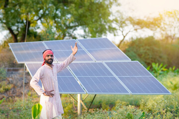 A confident indian farmer or rural worker stands in front of solar panels at agriculture field © PRASANNAPIX