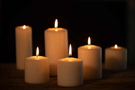 Group of White Pillar Candles Burning with Warm Glow on Wooden Surface