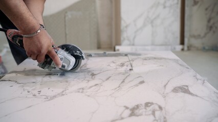 A construction worker uses an angle grinder to cut a large white marble or porcelain tile. Close up...
