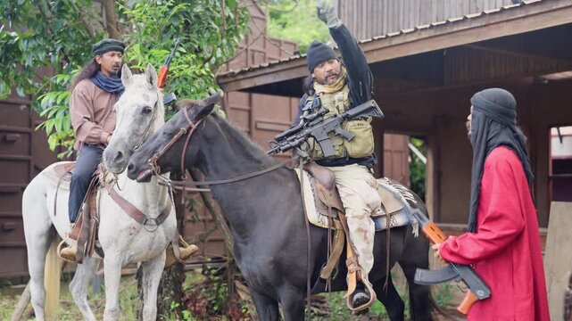 Close up the combatant man ride a horse to discuss and plan with his team to battle with the enemy in front of old building look like cowboy town.