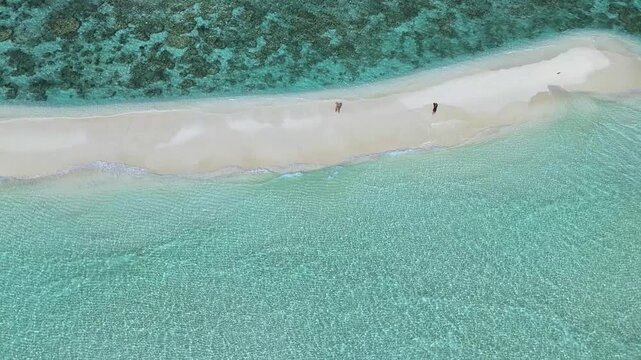 Aerial view of two people walking along a pristine white sandbar surrounded by crystal clear turquoise water and coral reefs in Thoddoo, Alif Alif Atoll, Maldives.