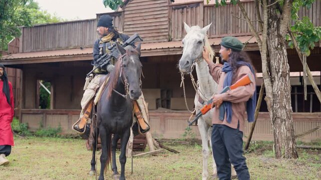 The combatant man ride a horse to discuss and plan with his team to battle with the enemy in front of old building look like cowboy town.