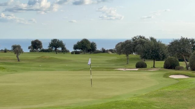 Panoramic golf course with lush green fairway stretches toward distant sea horizon framed by trees and sky. Scenic coastal golf landscape suits luxury resort promotion, Aphrodite Hills in Cyprus. 