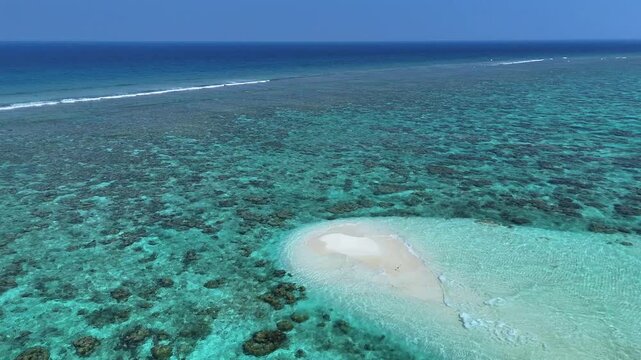 Aerial view of a small white sandbank surrounded by turquoise coral reefs and deep blue ocean in Thoddoo, Alif Alif Atoll, Maldives.