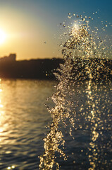 Fototapeta premium Atmospheric evening view of fountain water jet at sunset against pond. Golden reflections.