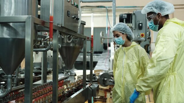 Two industrial engineer supervisors inspect and examine quality control, production process at automate conveyor in fish-canning food manufacturing factory, and protective uniforms for operations.