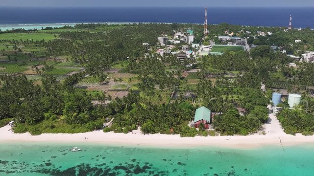 Aerial view of the lush tropical island of Thoddoo featuring white sandy beaches, turquoise waters, and dense palm groves in Thoddoo, Alif Alif Atoll, Maldives.