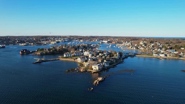 Aerial drone orbit of Gloucester Harbor, featuring Rocky Neck, Smith Cove and coastal residences under a clear blue sky, Massachusetts, USA