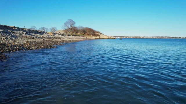 Drone footage skims the water's surface along a rocky Gloucester beach, Massachusetts, USA