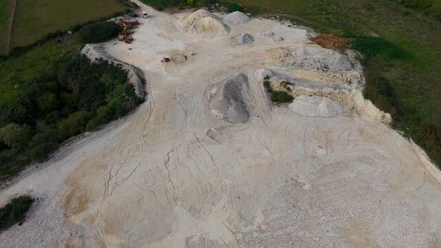 Sand and gravel quarry in Essendon seen from a rising drone with tilt-down reveal of aggregate stockpiles, haul roads, excavation benches, and surrounding countryside.