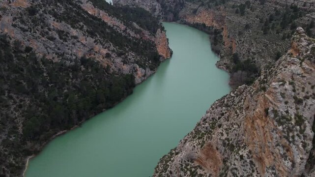 Aerial 4K view flying over the stunning turquoise J&uacute;car River in Spain, winding through a deep canyon with massive rocky cliffs and lush green vegetation on both sides in Castilla-La Mancha